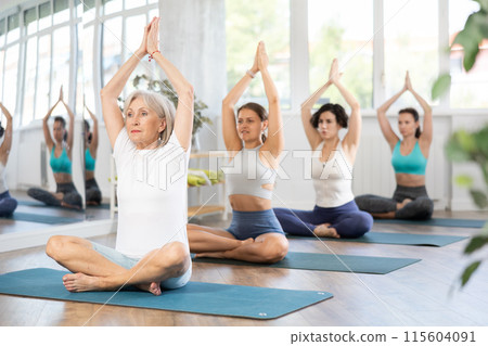 Elderly woman meditating in lotus pose during group yoga class 115604091