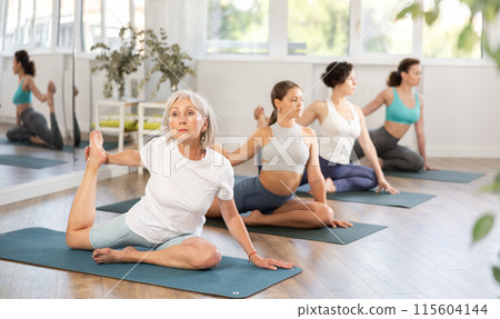 Group of women practicing yoga, working out doing version of Eka Pada Hasta Marjariasana in studio Group of women practicing yoga, working out doing version of Eka Pada Hasta Marjariasana in studio 115604144