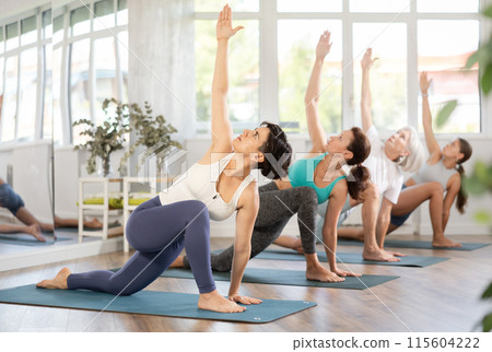 Hispanic woman performing revolved lunge pose in yoga studio 115604222