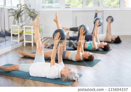 Group yoga or pilates classes - women lie on their backs with ball in their hands Group yoga or pilates classes - women lie on their backs with ball in their hands 115604337