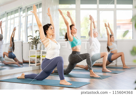 Woman performing revolved side angle pose Parivrtta Parsvakonasana during yoga class with female group in fitness studio Woman performing revolved side angle pose Parivrtta Parsvakonasana during yoga class with female group in fitness studio 115604368