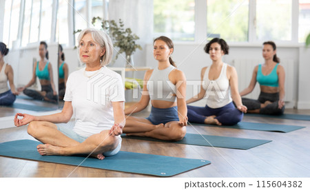 Senior woman sitting in Padmasana during group yoga training Senior woman sitting in Padmasana during group yoga training 115604382