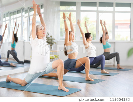 Senior woman performing Anjaneyasana at group yoga session Senior woman performing Anjaneyasana at group yoga session 115604383