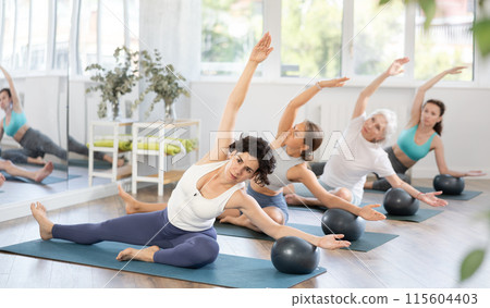 Group of women of different ages practicing yoga or pilates with balls in the gym of modern fitness studio. 115604403