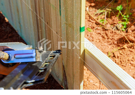 Working with an air pneumatic gun worker nails wooden fence during work 115605064