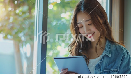 一位女士在窗邊的平板電腦上讀書 一位女士在窗邊的平板電腦上讀書 115605261