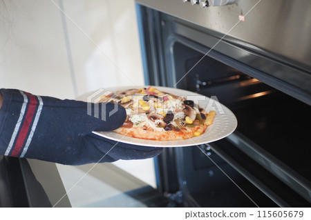 Person carefully using an oven mitt to remove a freshly baked pizza from the oven 115605679