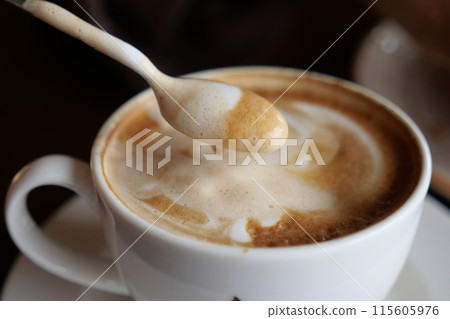 Enjoy a steaming hot cappuccino with swirling foam and a spoon for your delight 115605976