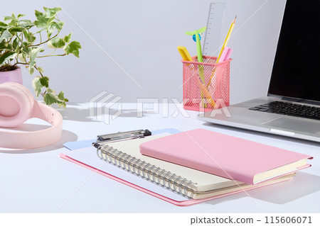 Office concept photo from front view, over white background. In the middle of white tabletop contains some notebook and clipboard, next to a laptop, pen pot, and a pink headphone. Space for designing Office concept photo from front view, over white background. In the middle of white tabletop contains some notebook and clipboard, next to a laptop, pen pot, and a pink headphone. Space for designing 115606071