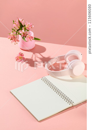 From above view photograph on pink background, a white notebook featured on pink table, next to a headphone and decorated with a flower vase. Copy space for adding text From above view photograph on pink background, a white notebook featured on pink table, next to a headphone and decorated with a flower vase. Copy space for adding text 115606080