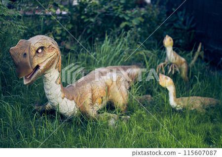 The oviraptor chick blinks its eyes against the background of grass. The effect of eye movement. A dinosaur is a small bird with a beak. High quality photo 115607087