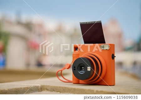 Vintage Orange Instant Camera in city with cloudy sky. Travel shooting equipment 115609038