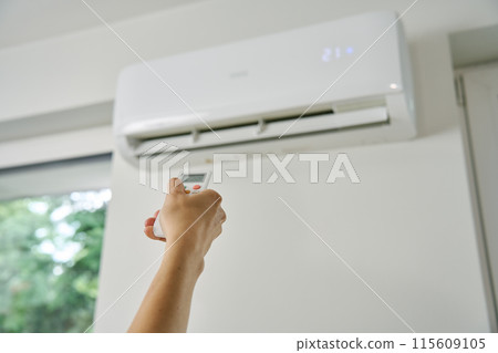 Adjusting air conditioner temperature with remote control. Hand holds remote control and setting comfortable temperature on climate system in apartment Adjusting air conditioner temperature with remote control. Hand holds remote control and setting comfortable temperature on climate system in apartment 115609105