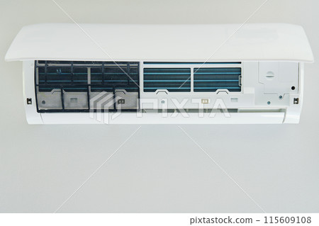White air conditioner unit is mounted on wall, ready for maintenance. Climate system with opened front cover revealing internal components. Repairing HVAC in apartment 115609108