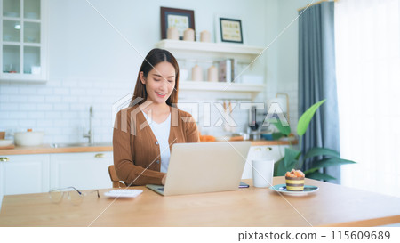Beautiful young Asian woman working with laptop computer in home kitchen. Work at home Beautiful young Asian woman working with laptop computer in home kitchen. Work at home 115609689