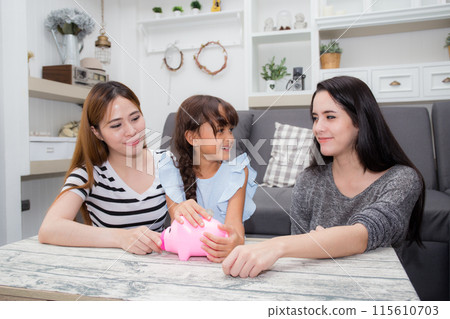 Mother teaching daughter saving with puts coins in piggy bank sitting on sofa in living room. Mother teaching daughter saving with puts coins in piggy bank sitting on sofa in living room. 115610703