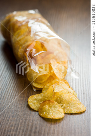 Crispy Potato Chips Spilled From  Plastic Bag on a Wooden Table 115610838