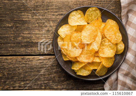 Crispy Potato Chips on plate on wooden table. Top view. 115610867