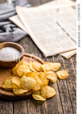 Crispy Potato Chips on cutting board on wooden table. 115610870