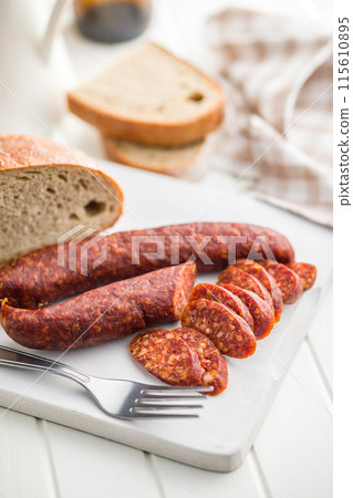 Sliced smoked salami sausage on wooden cutting board on white table. Sliced smoked salami sausage on wooden cutting board on white table. 115610895