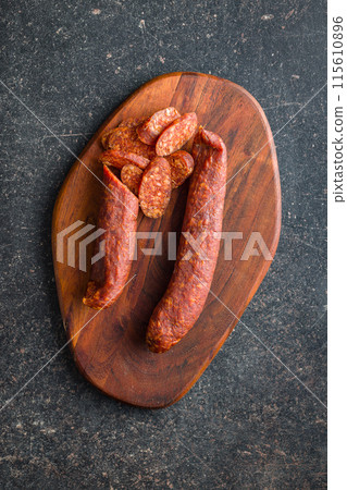 Sliced smoked salami sausage on wooden cutting board on black table. Top view. Sliced smoked salami sausage on wooden cutting board on black table. Top view. 115610896