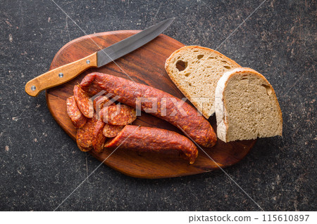 Sliced smoked salami sausage on wooden cutting board on black table. Top view. Sliced smoked salami sausage on wooden cutting board on black table. Top view. 115610897