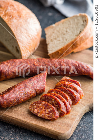 Sliced smoked salami sausage on wooden cutting board on black table. Sliced smoked salami sausage on wooden cutting board on black table. 115610903