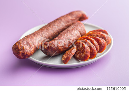Sliced smoked salami sausage on plate on violet background. Sliced smoked salami sausage on plate on violet background. 115610905