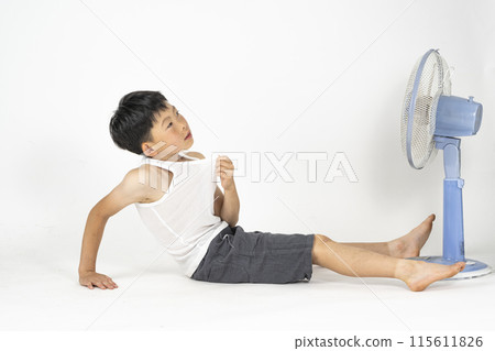 一名小學生在自己的房間裡穿著跑步襯衫，在風扇前感到酷熱，感到筋疲力盡。 115611826