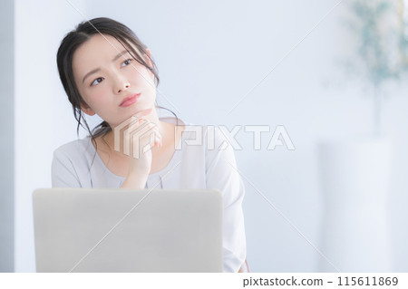 A young woman working on a computer, thinking and worrying, resting her chin on her hands A young woman working on a computer, thinking and worrying, resting her chin on her hands 115611869