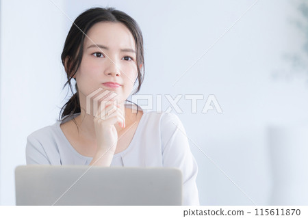 一位年輕女子在電腦上工作，擺出憂心忡忡的姿勢托著下巴 115611870