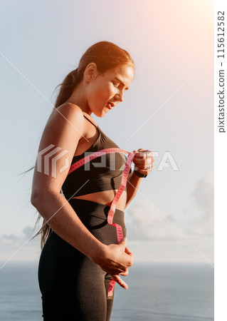 A woman is holding a pink tape measure and is measuring her breasts after morning fitness A woman is holding a pink tape measure and is measuring her breasts after morning fitness 115612582