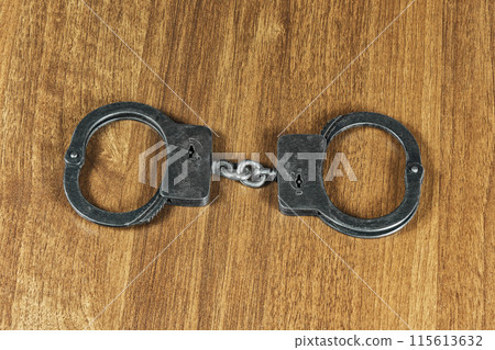 Police handcuffs lie on a wooden table Police handcuffs lie on a wooden table 115613632