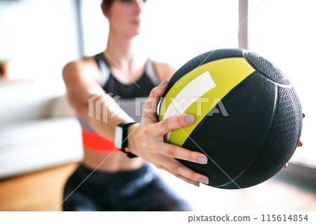 Beautiful redhead woman's home workout routine with medicine ball. Home fitness workout in living room, sporty woman wearing sportswear. Beautiful redhead woman's home workout routine with medicine ball. Home fitness workout in living room, sporty woman wearing sportswear. 115614854