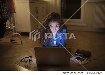 A beautiful university student having evening online class, e-learning sitting at home. Online consultation. A beautiful university student having evening online class, e-learning sitting at home. Online consultation. 115614924