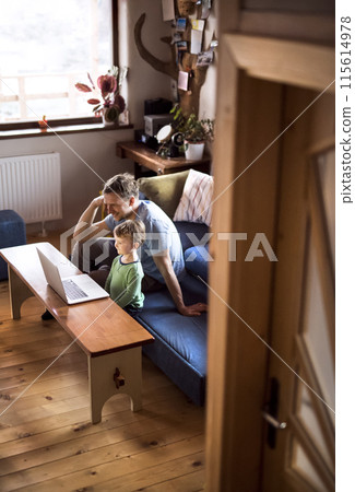 Dad and boy watching cartoons on laptop, sitting on sofa in living room, having great time together. Dad and boy watching cartoons on laptop, sitting on sofa in living room, having great time together. 115614978
