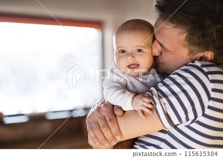 Handsome dad holding small baby, carrying him around house. Unconditional paternal love, father's Day concept. 115615384