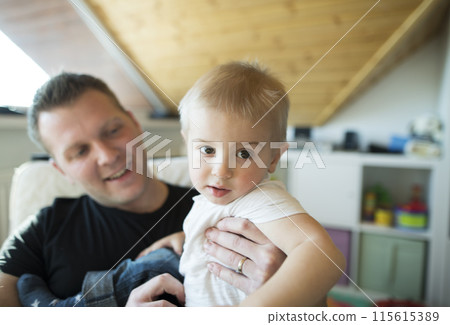 Father holding his son in arms, spending time with toddler in his room. Unconditional paternal love, Father's Day concept. 115615389