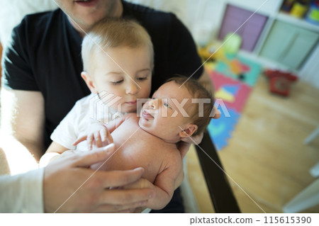 Father helping his son to hold little baby sister. Dad spending time with kids in room. Unconditional paternal love, Father's Day. 115615390