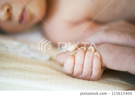 Parent holding small hand of little baby lying on bed. Parent holding small hand of little baby lying on bed. 115615409