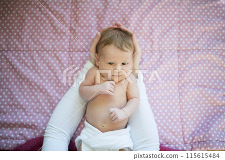 Portrait of cute little baby lying on bed, parents hands holding her. Portrait of cute little baby lying on bed, parents hands holding her. 115615484