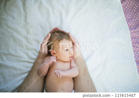 Portrait of cute little baby lying on bed, parents hands holding her. Portrait of cute little baby lying on bed, parents hands holding her. 115615487
