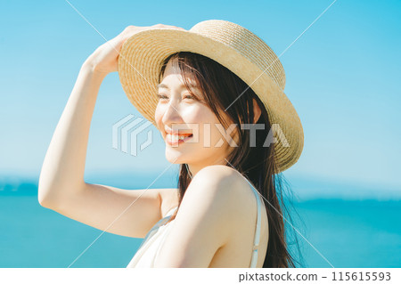A woman wearing a straw hat with the sea and blue sky in the background 115615593