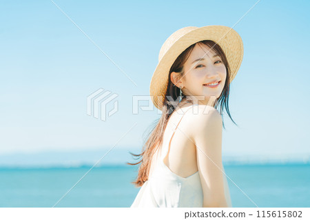 A woman wearing a straw hat with the sea and blue sky in the background 115615802