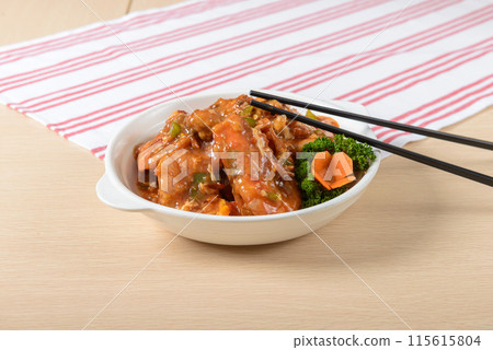 A bowl of Prawn with chopsticks on a table. The food is a mix of meat and vegetables, and the chopsticks are placed on top of the food 115615804