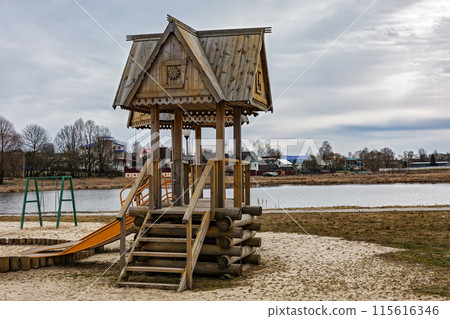 A wooden arbor of logs stands on the shore of a pond. On the shore of the pond there is a wooden gazebo with a staircase 115616346