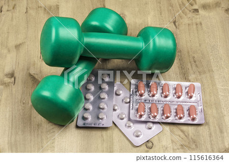 Two dumbbells and tablets lie on a wooden surface 115616364