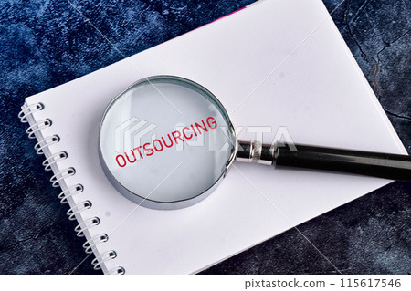 Copy space. Business concept. OUTSOURCING symbol written through a magnifying glass in a notebook on a beautiful blue heterogeneous background 115617546