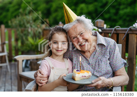 Granddaughter celebrating birthday with elderly grandma, holding cake with candle. Senior lady spending time with young girl, enjoying together time. 115618380