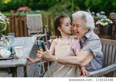 Granddaughter taking selfie with elderly grandma, companionship. Senior lady spending time with young girl, enjoying together time. 115618386
